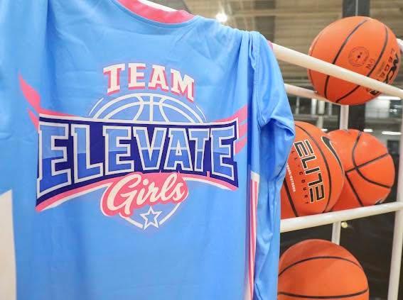 A light blue Team Elevate jersey hanging beside a rack of basketballs.