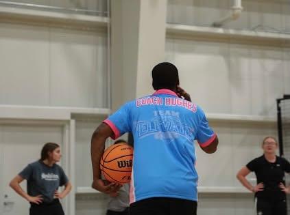 Coach Hughes, seen from behind in a Team Elevate shirt, holds a basketball.