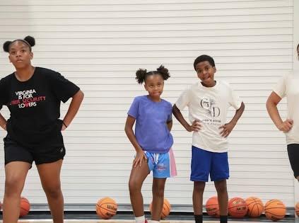 Four young players stand side by side in front of a row of basketballs.